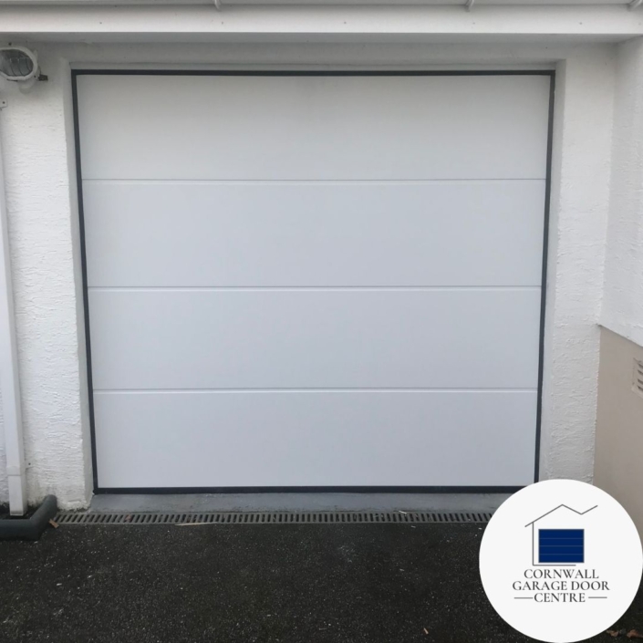 An image showcasing a sleek, white insulated sectional door with a smooth surface design. The door's clean lines and solid construction provide both aesthetic appeal and energy efficiency. Ideal for modern homes and commercial spaces.